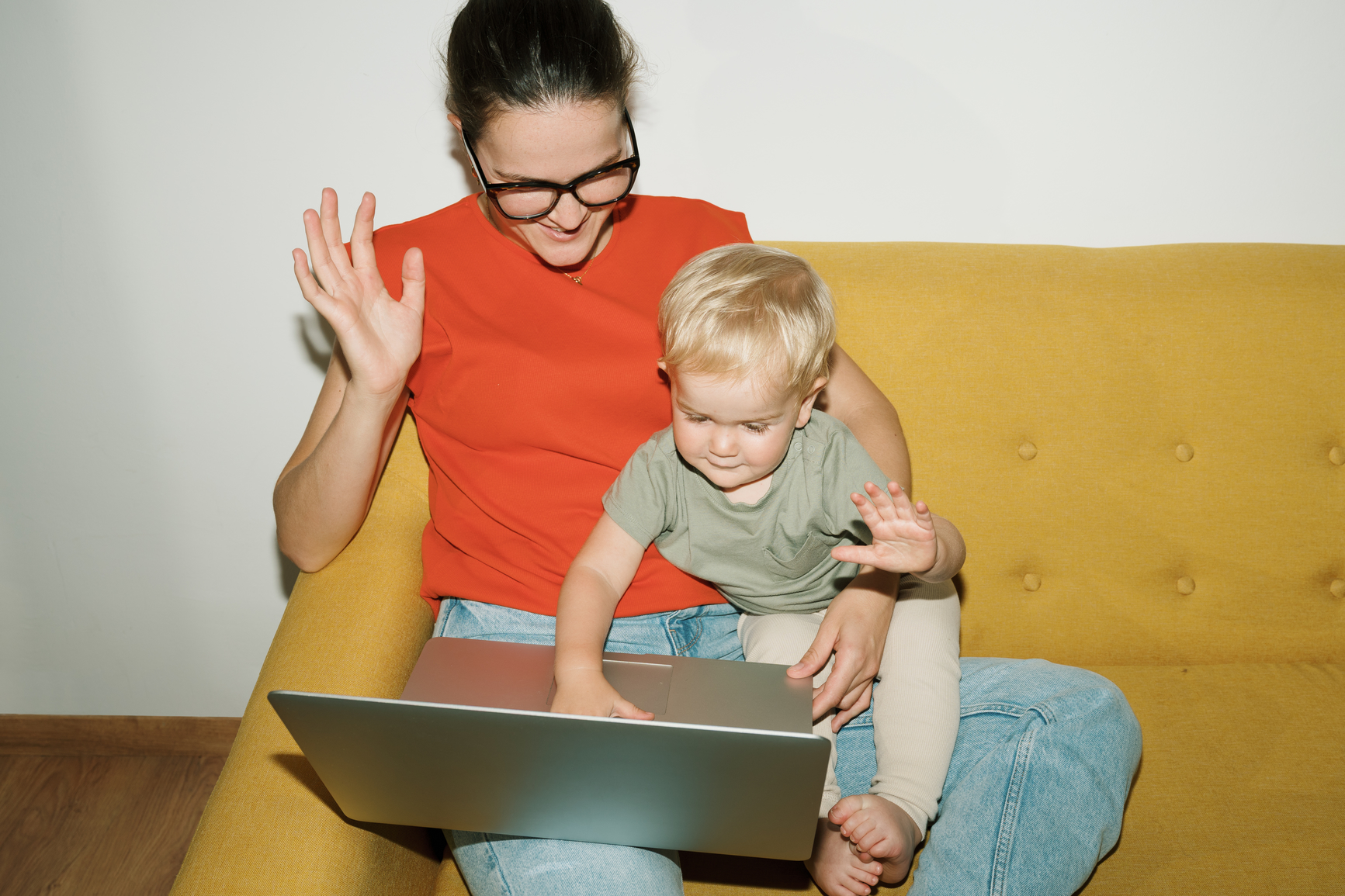 Mom and her toddler sharing a laptop on a yellow couch